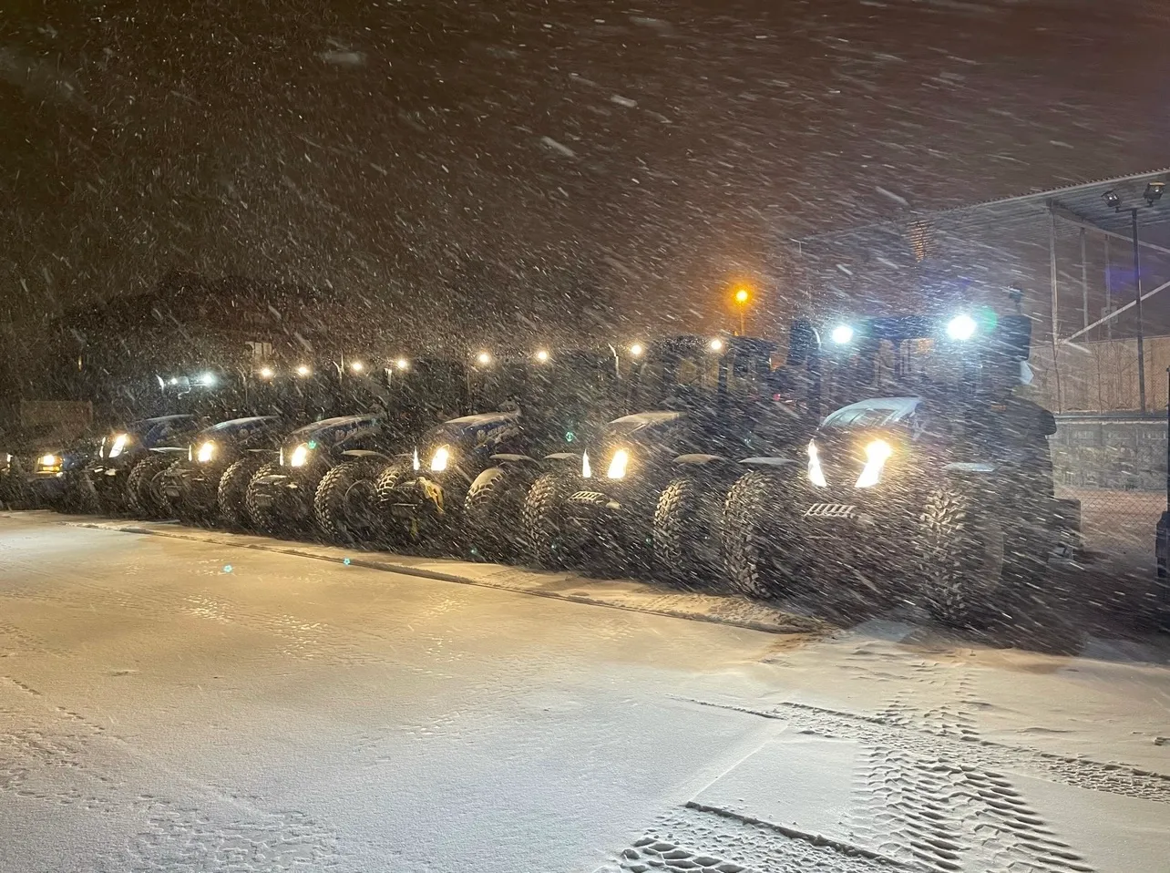 Snow-removal tractors lined up during a heavy nighttime snowfall.