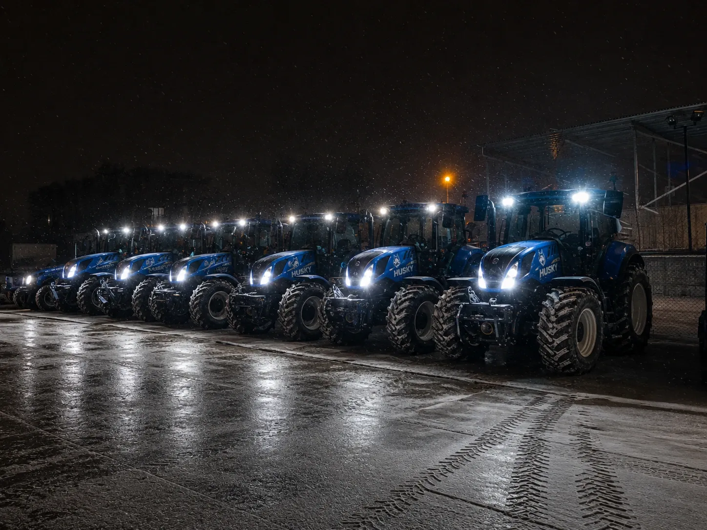 Blue Husky snow-removal tractor fleet lined up during a nighttime snowfall.